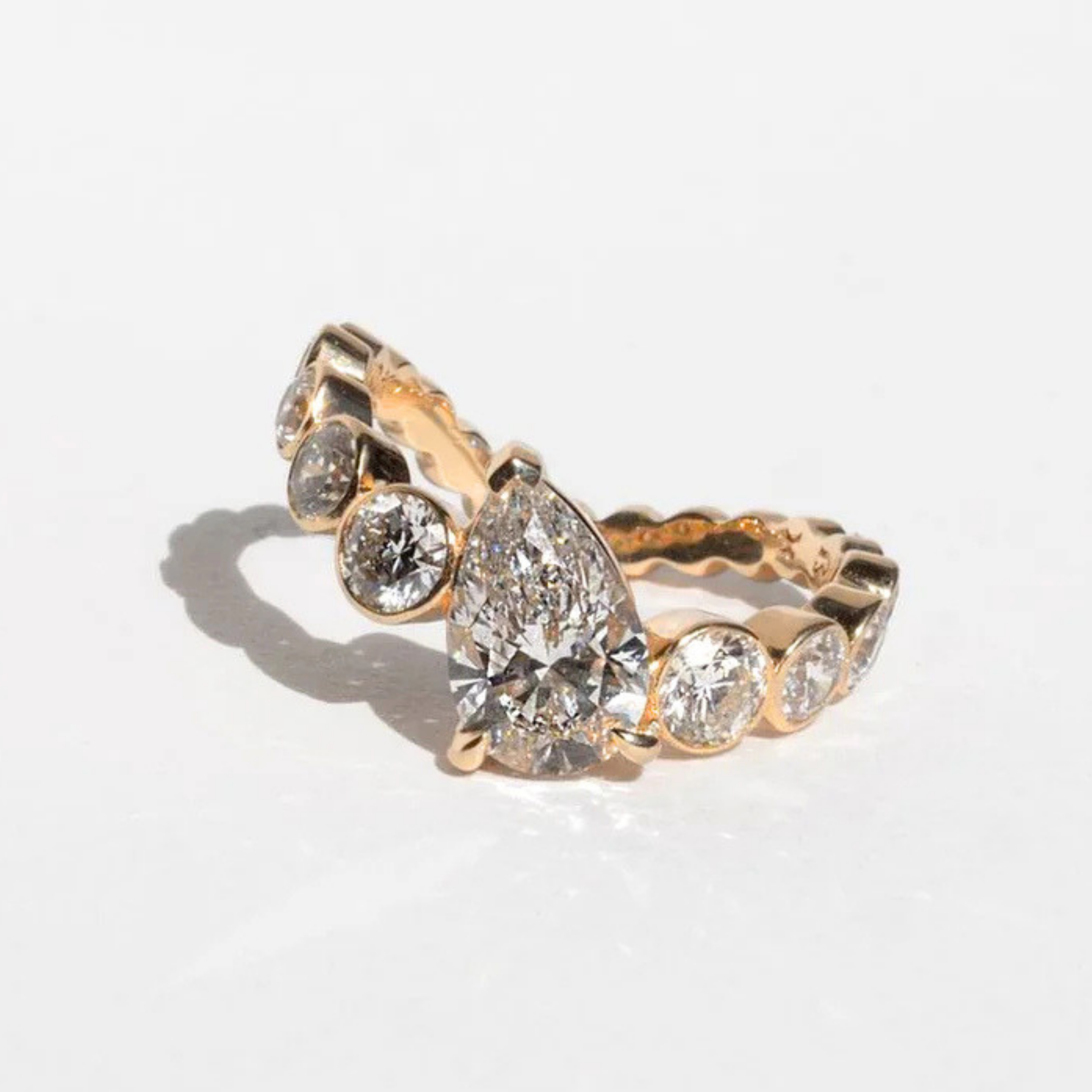 Pear diamond engagement ring with curved bezel-set round diamond band in yellow gold by ARIAH BELVI